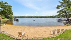 A lakeside view with a sandy beach, chairs, and docked boats. - Sandy Toes at Lighthouse Cove (Wisconsin Dells)
