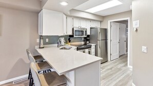 A modern kitchen with white cabinets, a stainless steel refrigerator, a microwave, and a gas stove. - Sandy Toes at Lighthouse Cove (Wisconsin Dells)