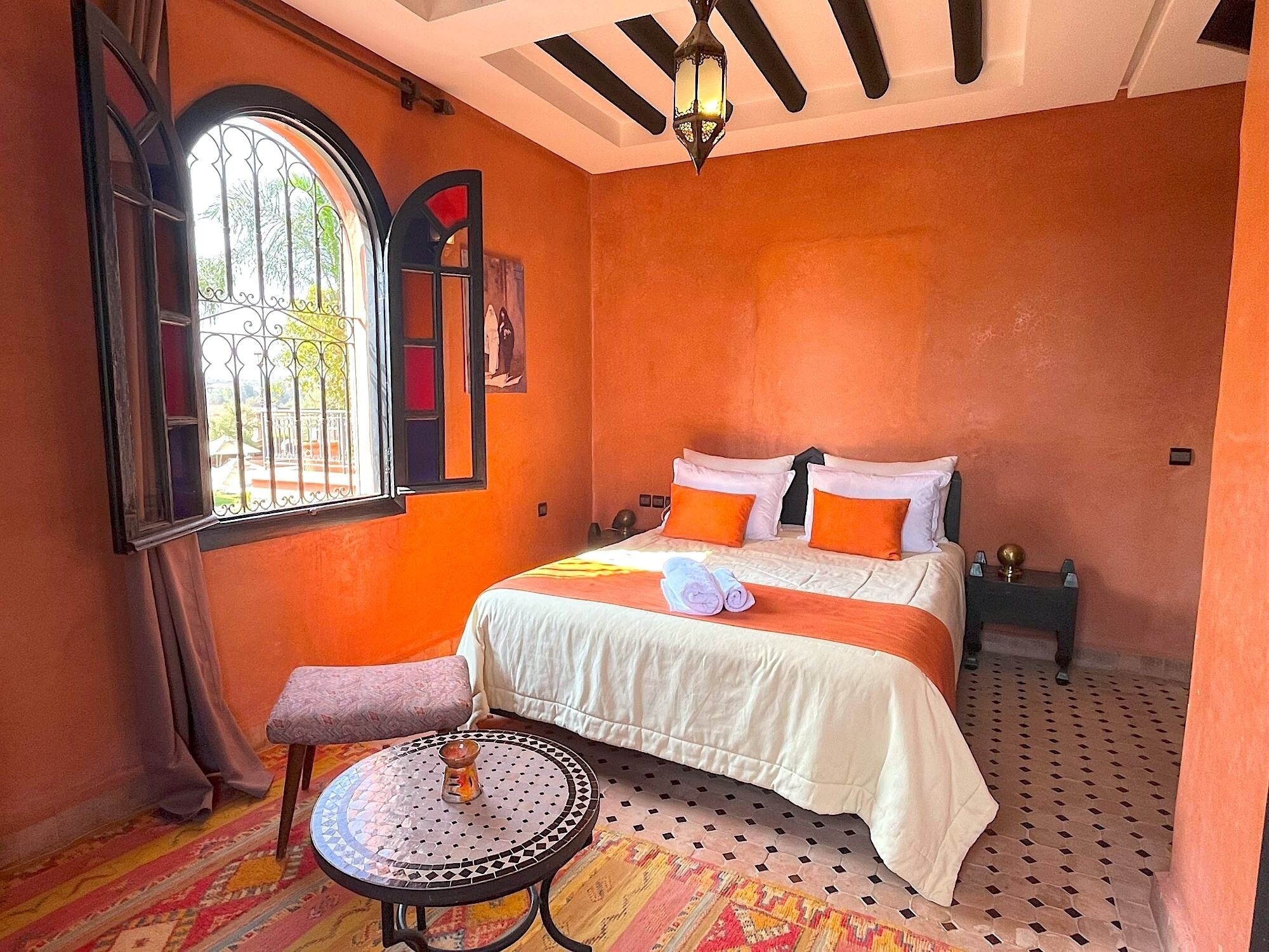 A room with a bed, a small table, a window with a view, and a decorative wall piece.