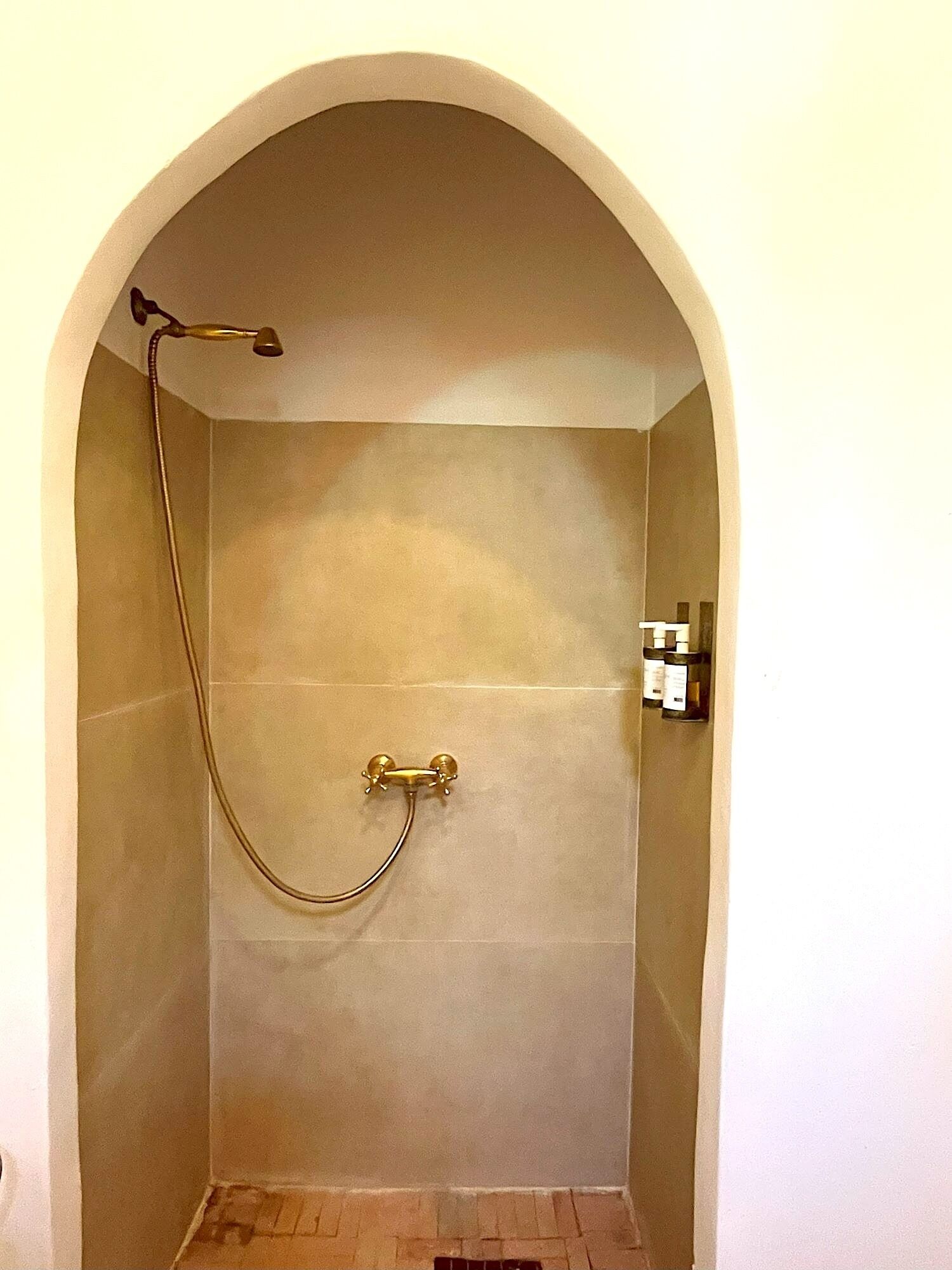 A small, arched shower room with a single showerhead and a handheld shower attachment.