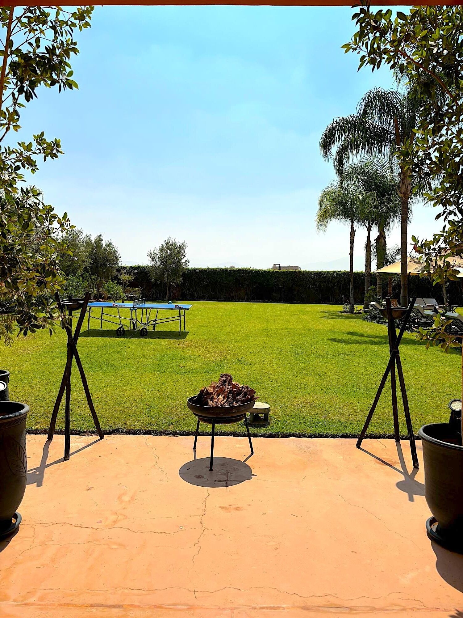 A patio with a barbecue grill, outdoor seating, and a view of a tennis court.