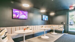 A modern lounge area with a sofa, two round tables, and a TV screen on the wall.