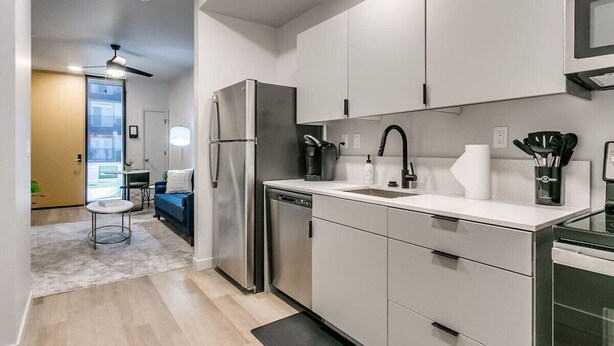 A modern kitchen with stainless steel appliances, white cabinetry, and a small dining area with a blue sofa.