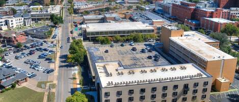 An aerial view of a cityscape with a large building featuring a flat roof and multiple windows, surrounded by parking lots and other buildings.
