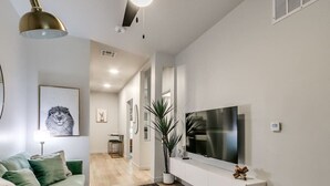 Una sala de estar moderna con un sofá, un televisor de pantalla plana montado en la pared, una planta en maceta y un tapete de diseño.