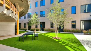 Un patio con césped artificial, dos árboles y mobiliario para exteriores.