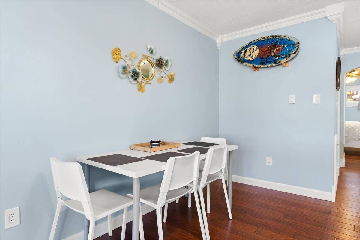 Uma área de refeições com mesa e cadeiras brancas, um objeto decorativo na parede e um skate.