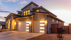 A modern two-story house with a stone facade, two garages, and a well-lit driveway. - Escape to your own private oasis in sunny Washington, Utah! (Washington)