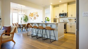 A modern kitchen with a central island, bar stools, and a dining area with chairs and a table. - Escape to your own private oasis in sunny Washington, Utah! (Washington)