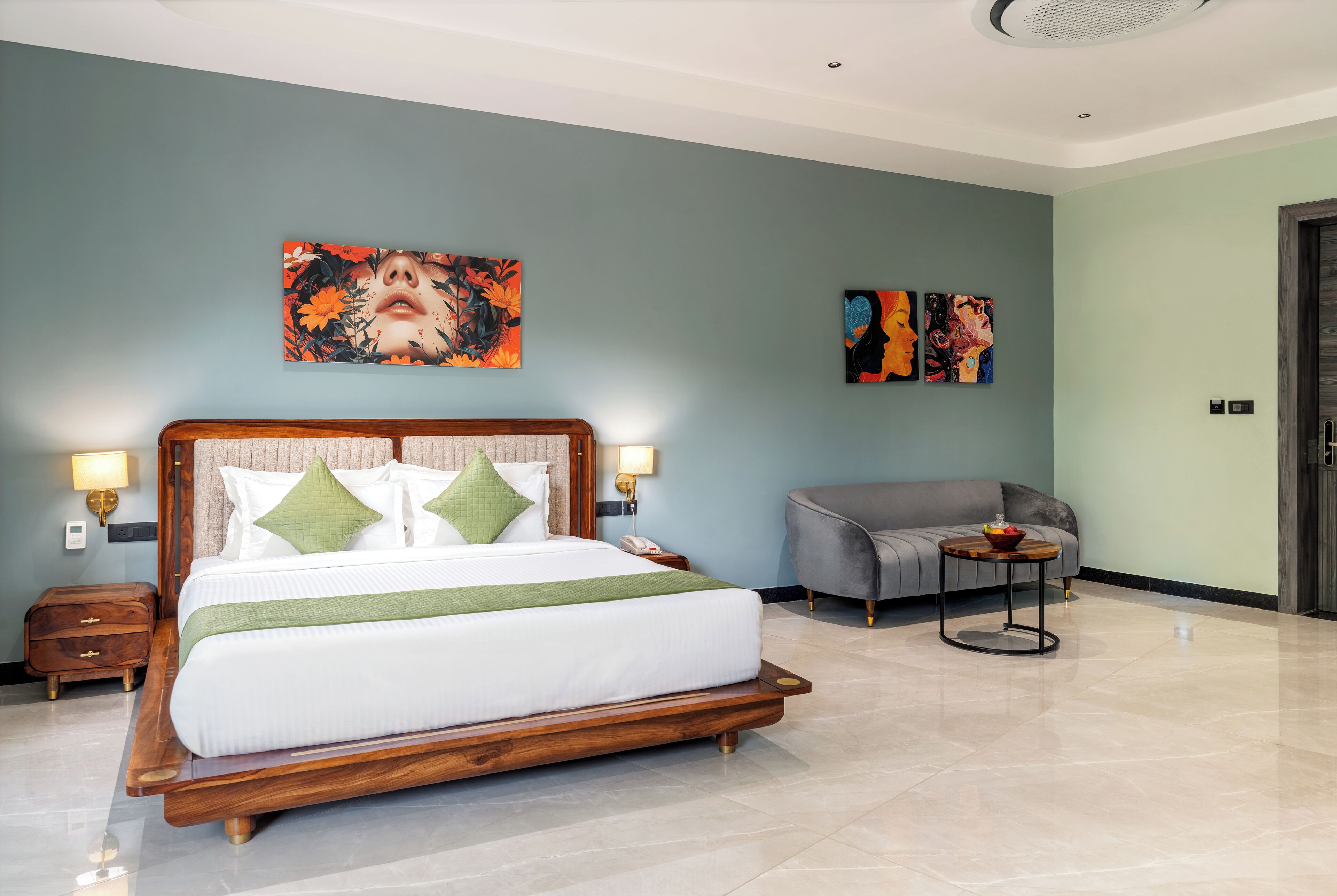 Habitación de hotel moderna con una cama grande, un sofá gris y obras de arte en las paredes.