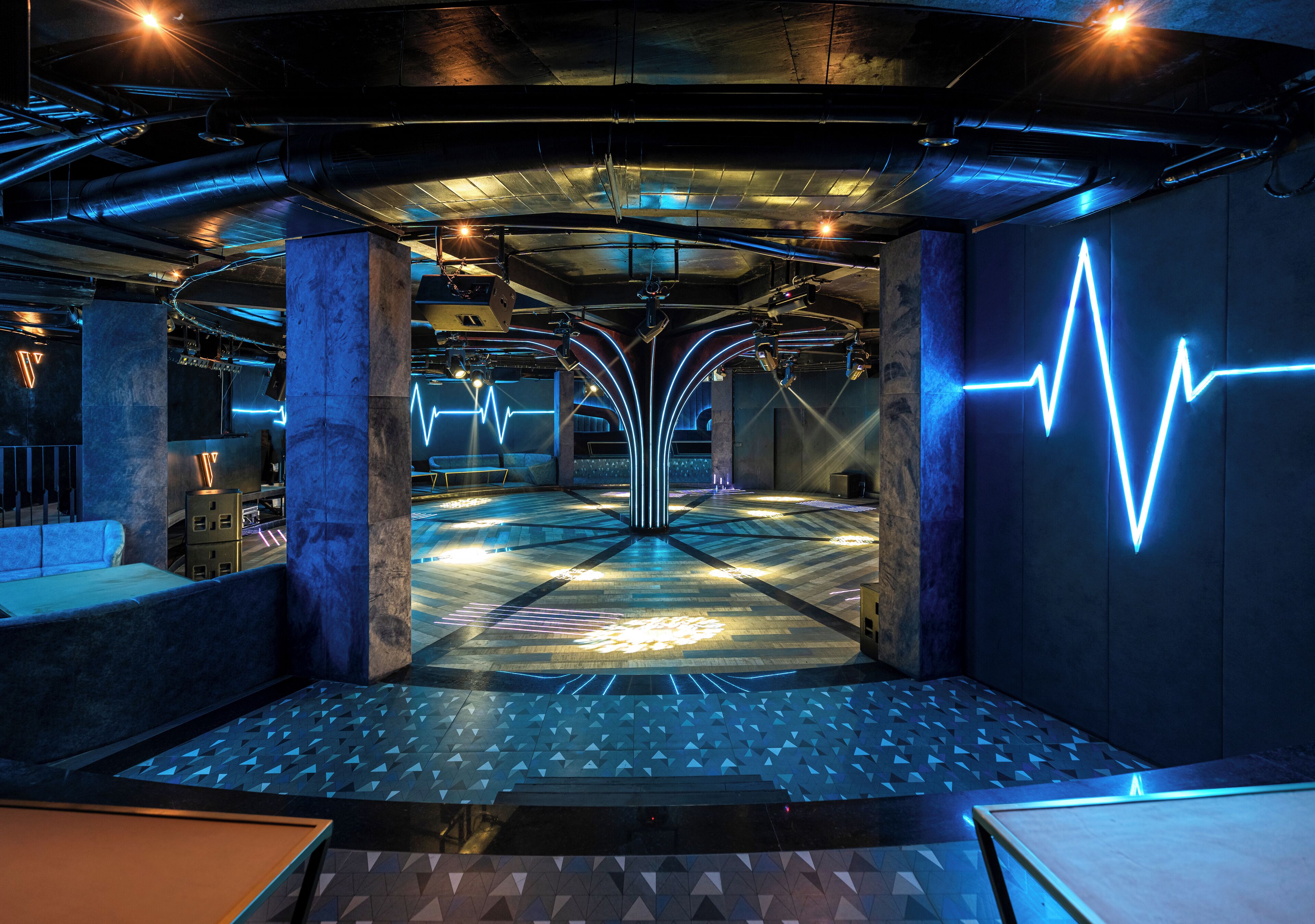 A modern interior with a central open space, multiple seating areas, and a prominent light installation on the wall.