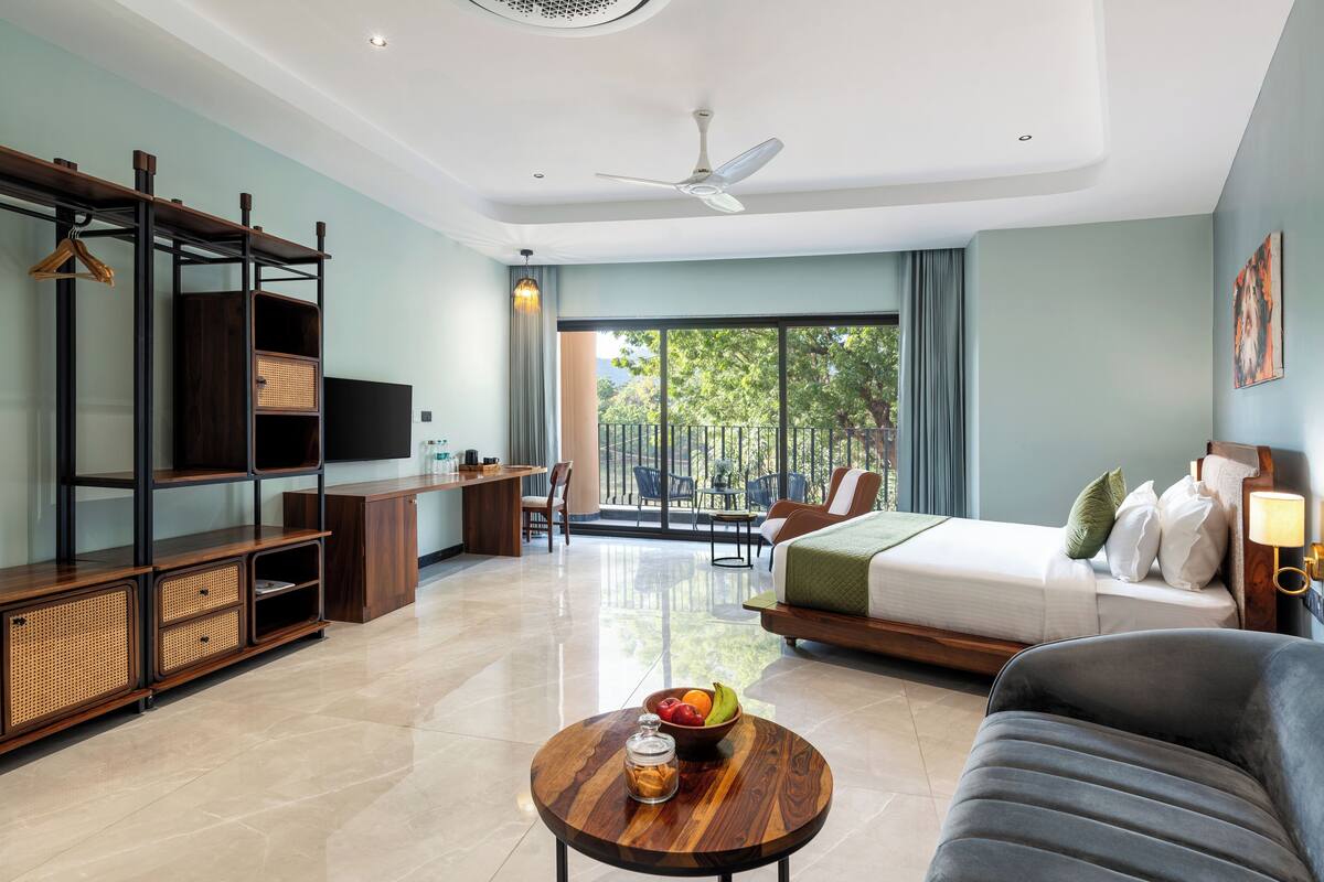 A modern hotel room with a bed, sofa, TV, desk, and balcony.