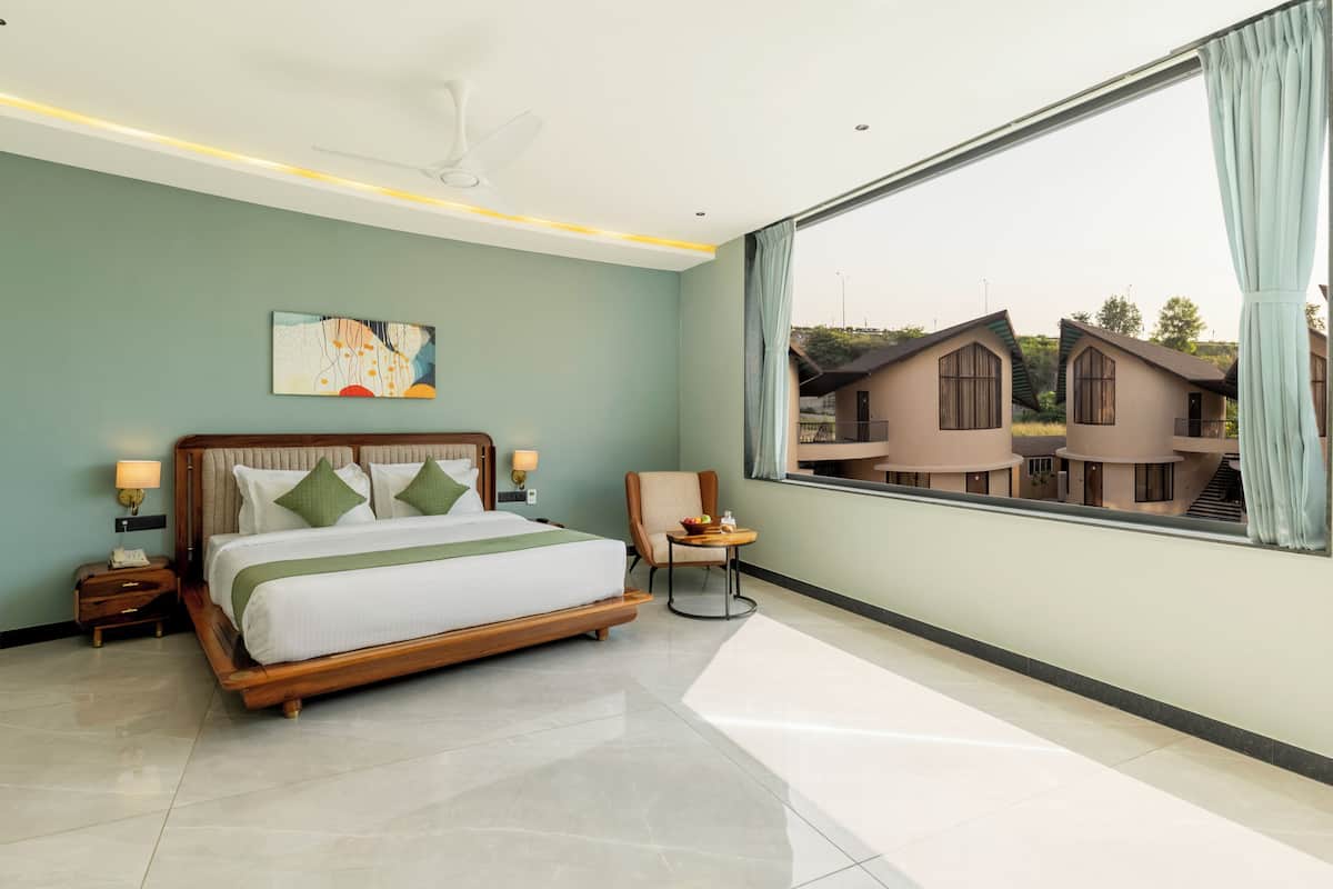 A modern bedroom with a large bed, a chair, a small table, and a view of other buildings.