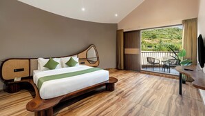 A modern bedroom with a curved wooden bed, a balcony with outdoor seating, and a view of greenery. - The Qualia Resort Club & Brewery (Udaipur)