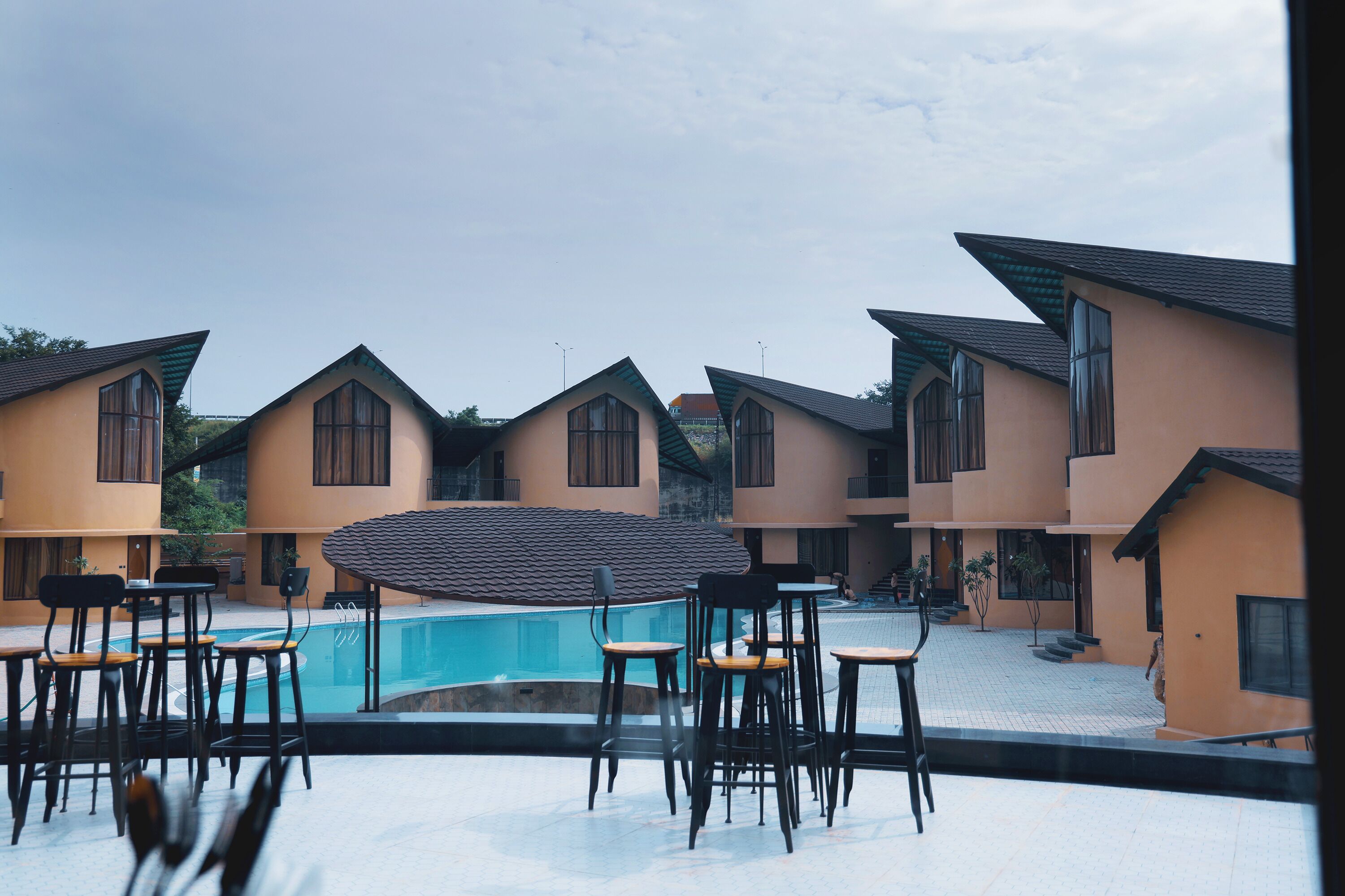 A poolside area with multiple tables and chairs, a swimming pool, and a series of buildings with a consistent architectural style.