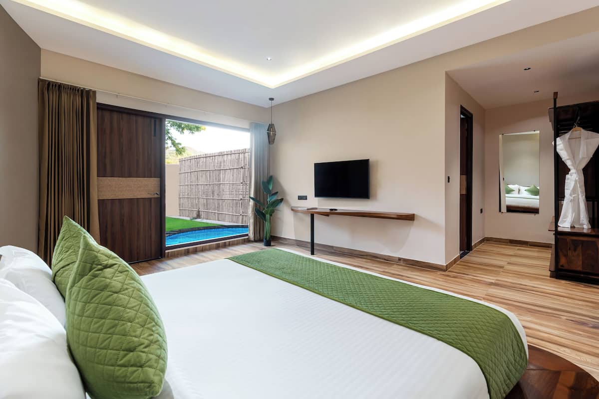 A modern hotel room with a large bed, a TV mounted on the wall, and a sliding door leading to an outdoor area.