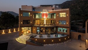 A modern hotel with a central courtyard, multiple floors, and a distinctive red light sculpture. - The Qualia Resort Club & Brewery (Udaipur)
