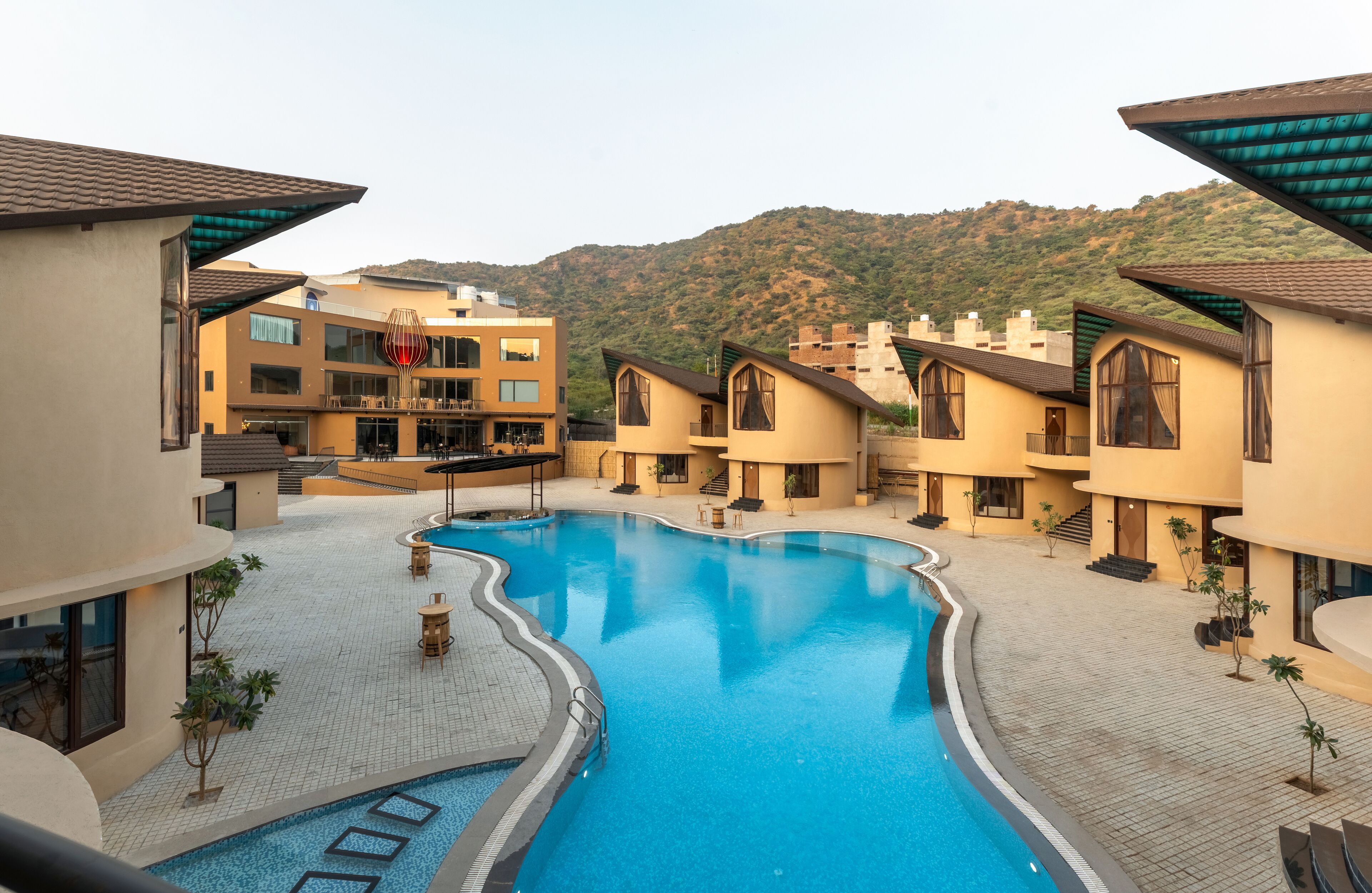 A resort with a swimming pool, multiple buildings, and a mountainous backdrop.