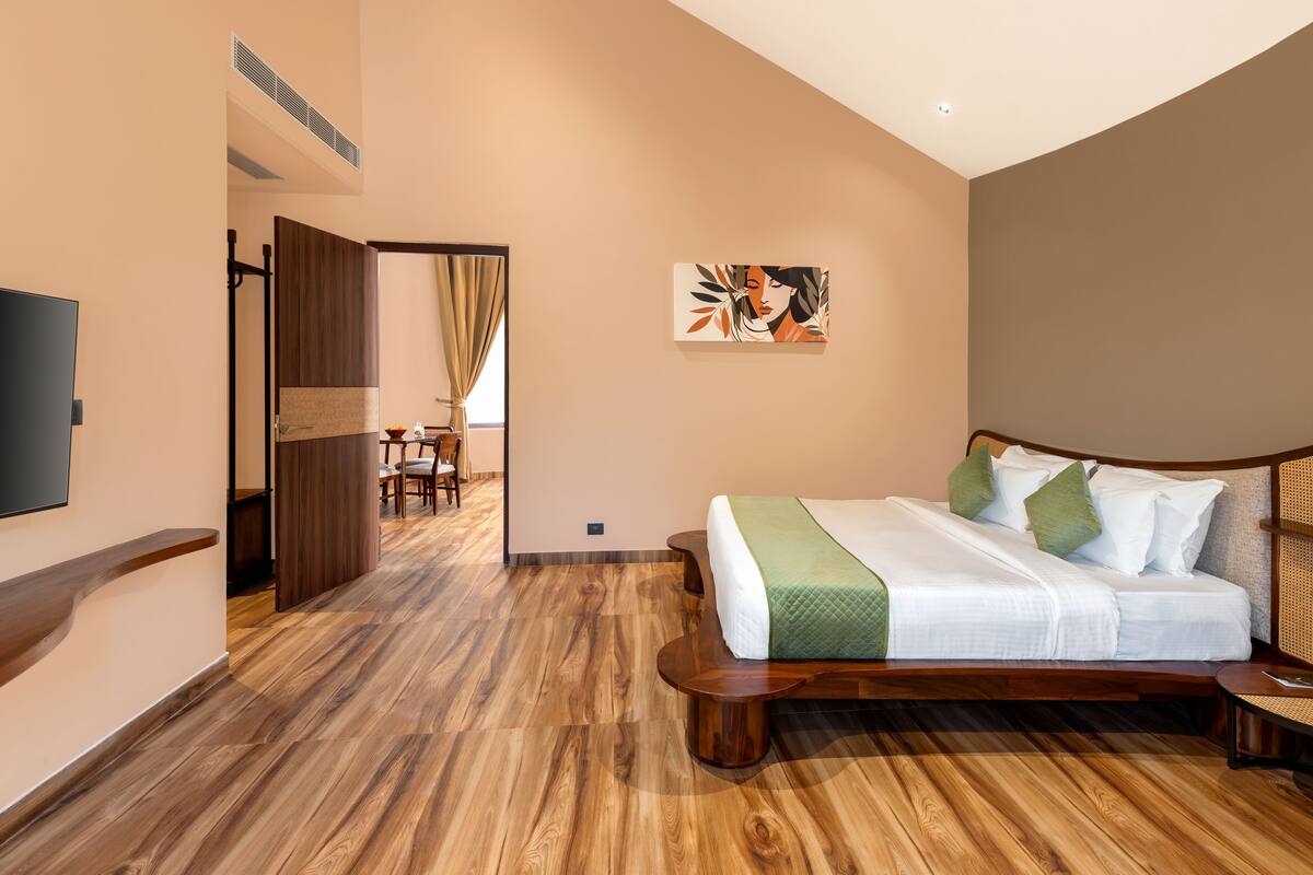 A modern hotel room with a wooden floor, a large bed with green and white bedding, a flat-screen TV, and a painting on the wall.