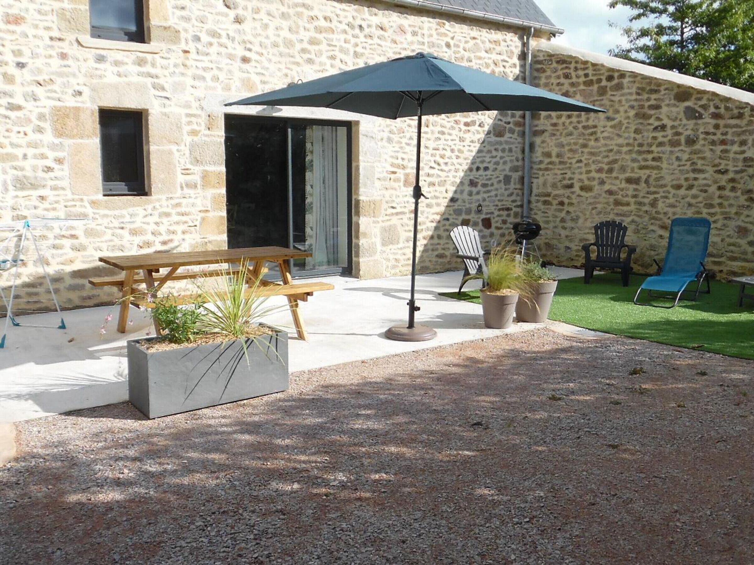 A stone building with a wooden picnic table and an umbrella, surrounded by potted plants and outdoor seating.
