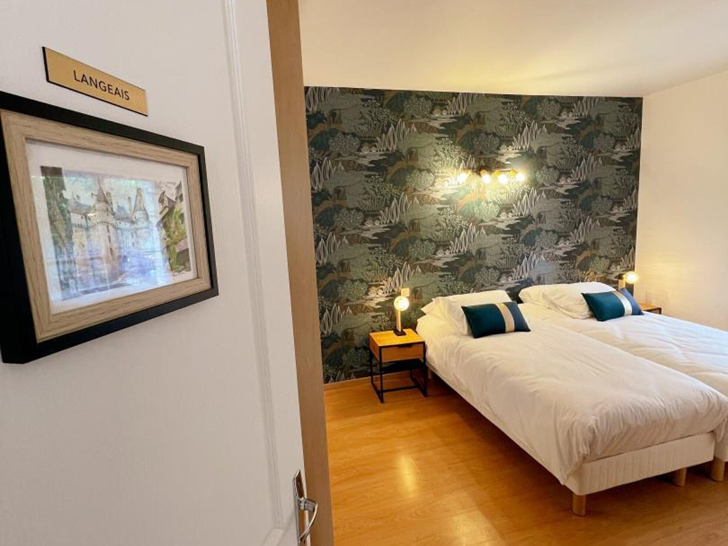 A hotel room with a bed, a nightstand, a wall-mounted lamp, and a framed picture.