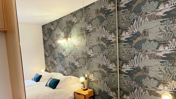 Ein Schlafzimmer mit einem Bett, Nachttischen und einer Wand mit Wandpapier mit Naturmotiv.