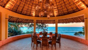 A dining area with a thatched roof, overlooking the ocean.