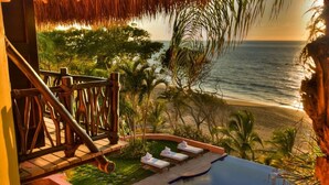 A poolside area with a view of the ocean, a thatched roof, and lounge chairs.