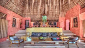A lobby with a thatched roof, a central seating area with cushions, and a staircase leading to upper floors.