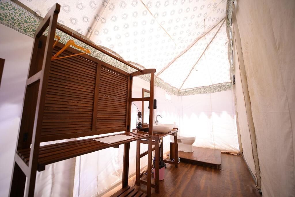 Habitación tipo tienda de campaña, compacta y bien iluminada, con una cama litera de madera, un lavamanos pequeño y un perchero.