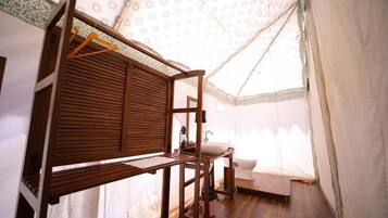 Habitación tipo tienda de campaña, compacta y bien iluminada, con una cama litera de madera, un lavamanos pequeño y un perchero.