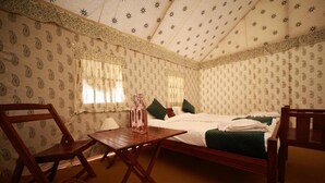 Ein Zimmer mit einem Bett, zwei Stühlen, einem kleinen Tisch und einem Fenster mit Vorhängen.