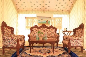 A room with a floral sofa set, wooden chairs, a coffee table, and a patterned rug.