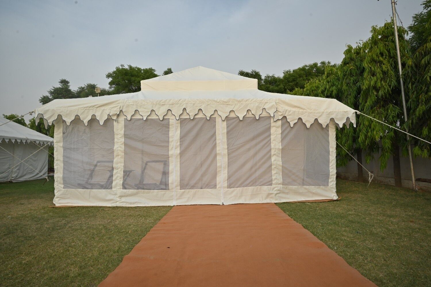 A white tent with a red carpet leading to it, set on a grassy area with trees in the background.