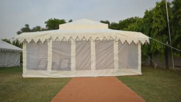 A white tent with a red carpet leading to it, set on a grassy area with trees in the background.