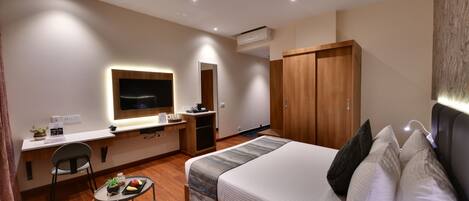Habitación de hotel con cama, escritorio, silla, televisor y armario.