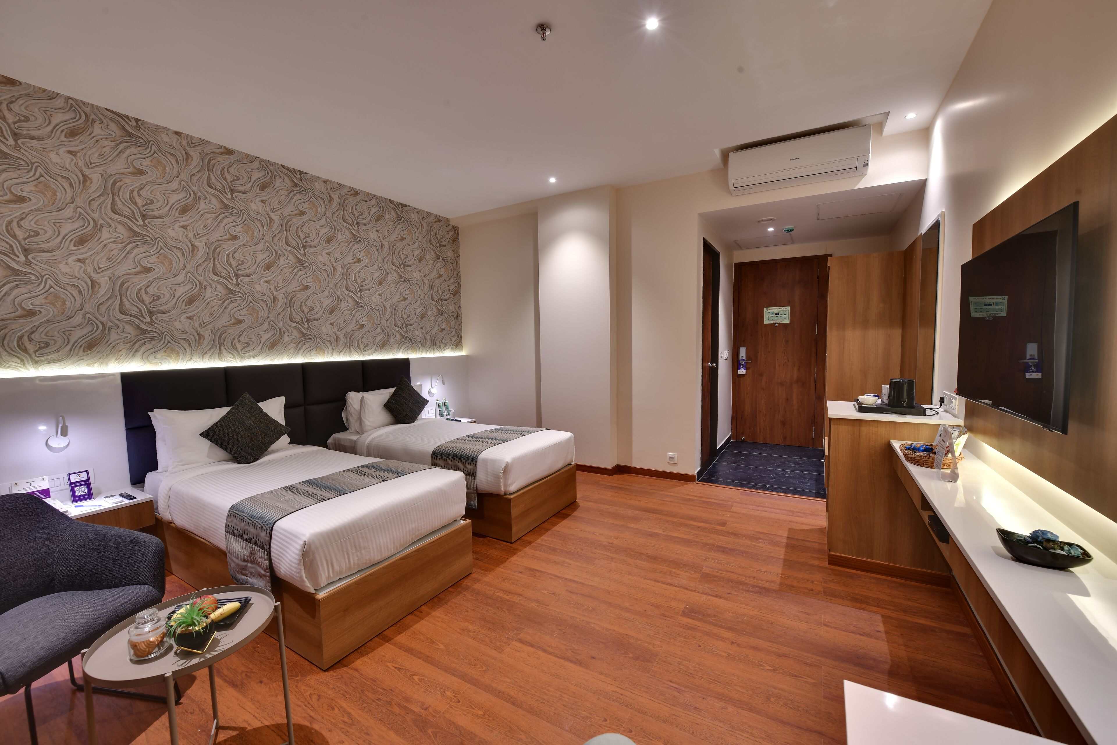 Habitación de hotel con dos camas, un escritorio, una silla, una mesita con una planta y un televisor.