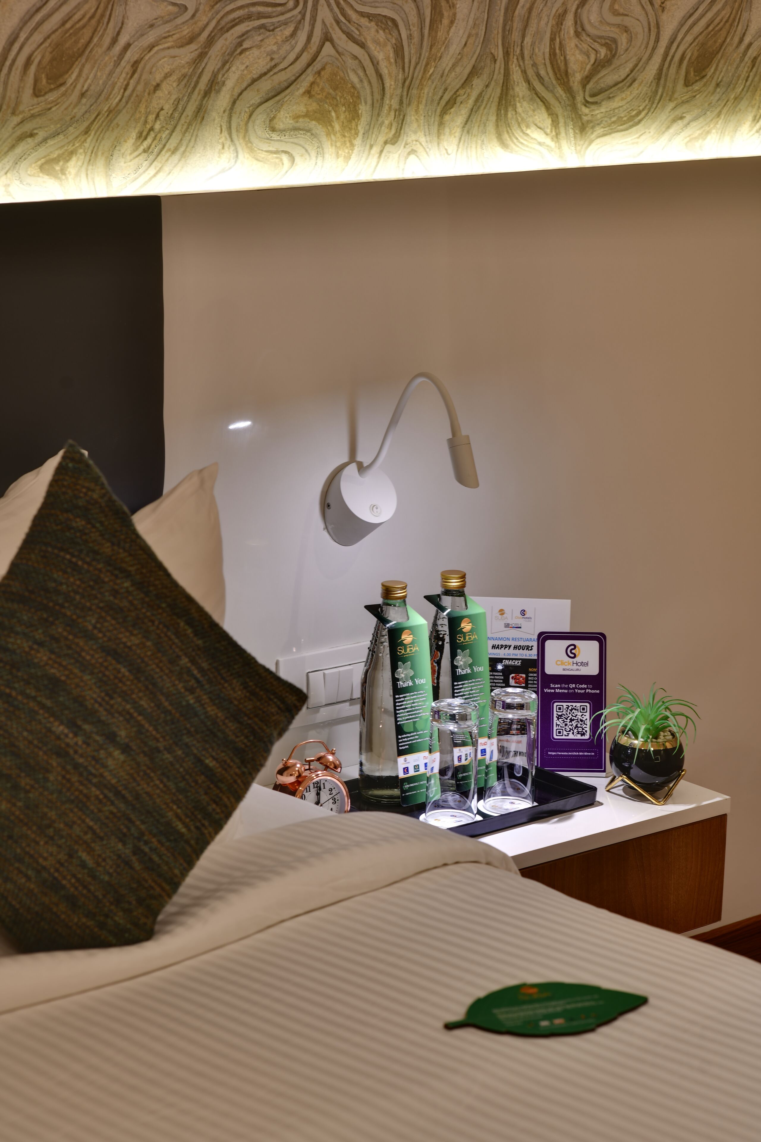A hotel room with a bed, pillows, a nightstand with a lamp, a clock, and a QR code for the City Hotel.