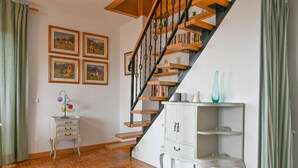 Una escalera con peldaños de madera y barandillas negras, flanqueada por cuadros en las paredes.