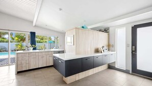 A modern kitchen with light wood cabinets, dark countertops, and a large island. - Mountain-View Retreat: Pet-Friendly Home with Private Pool (Palm Springs)