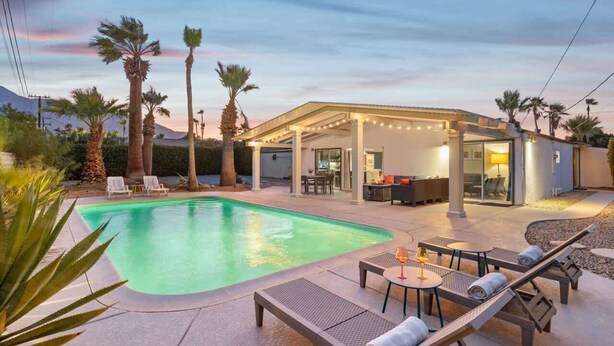 A modern outdoor pool area with lounge chairs, a covered seating area, and palm trees. - Mountain-View Retreat: Pet-Friendly Home with Private Pool (Palm Springs)