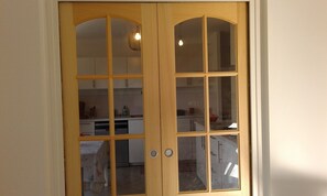 Una puerta doble de madera con paneles de vidrio, que da a una cocina con armarios y encimera.