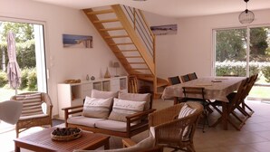 Una zona de comedor con una mesa y sillas de madera, una escalera y un sofá con cojines.