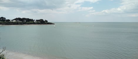 Vista costera con aguas tranquilas, una playa arenosa y una pequeña isla con edificios.