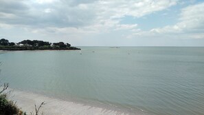 Une vue sur la côte, avec des eaux calmes, une plage de sable et une petite île parsemée de bâtiments.
