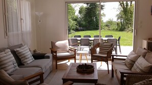 Una sala de estar con sofá, sillas, una mesa de centro y vistas a un jardín a través de un ventanal corredera.