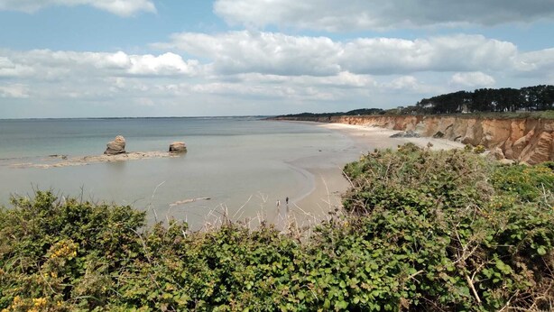 Un paisaje costero con una playa arenosa, afloramientos rocosos y un acantilado con vegetación.