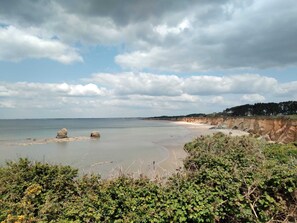 Ett kustlandskap med en sandstrand, klippformationer och en klippa med växtlighet.