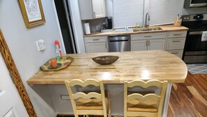 Una cocina con una isla de madera, dos sillas, una cafetera, un fregadero y un lavavajillas.