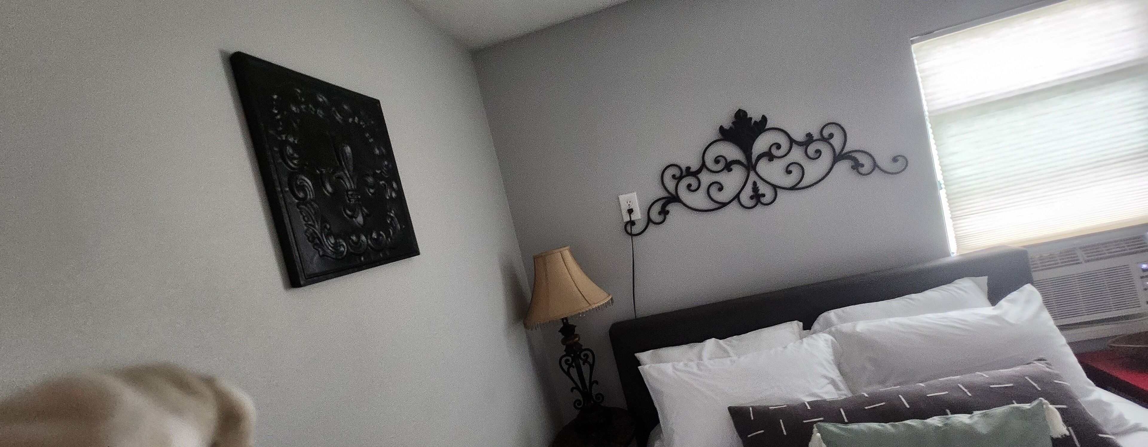A hotel room with a bed, a wall-mounted decorative piece, a lamp, and a window with blinds.